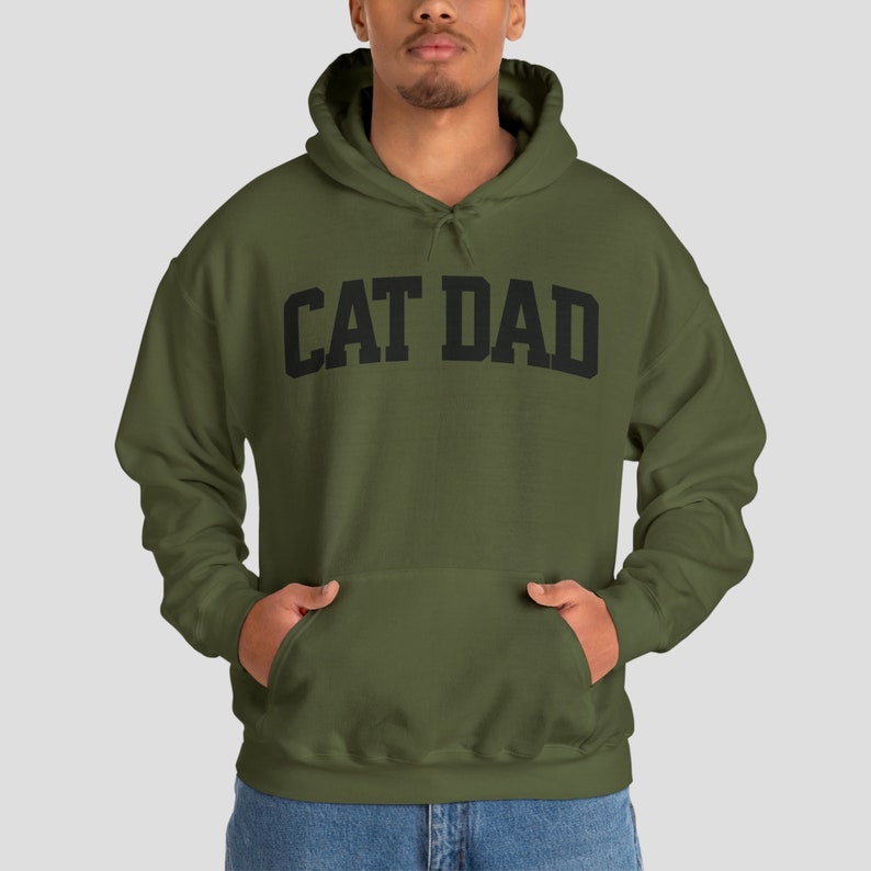 Military Green colored pullover hoodie with Cat Dad printed in an arch on the front in black.  Varsity athletic block style font printed on the hooded sweatshirt.
