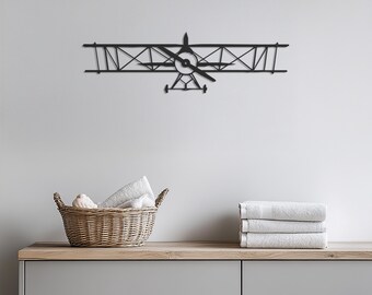 May include: A black metal biplane wall art piece. The airplane features a propeller and detailed wing design. The image also shows a wicker basket with towels and a stack of folded white towels on a wooden surface.