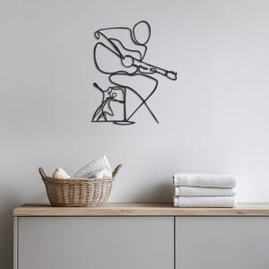 May include: Black metal wall art depicting a person playing a guitar. The art is in a minimalist style with a single line drawing.