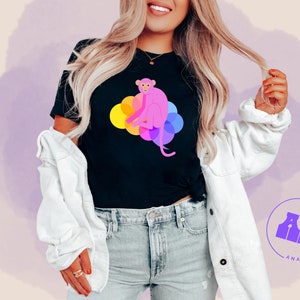 May include: A black t-shirt featuring a pink monkey sitting on a rainbow of colourful circles. The text "Analog Frog" is in a purple circle below the monkey.