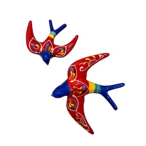 May include: Two red ceramic swallows with blue and yellow accents. The swallows are flying in opposite directions.