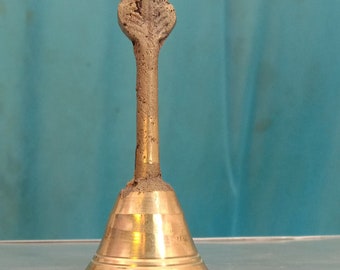 May include: A gold-colored bell with a decorative top, sitting on a gray surface.