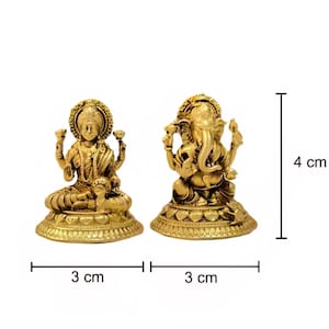 Pode incluir: Duas est&aacute;tuas douradas das divindades hindus, Lakshmi e Ganesha, s&atilde;o exibidas sobre um fundo branco. Lakshmi est&aacute; sentada, e Ganesha &eacute; retratado com uma cabe&ccedil;a de elefante. Cada est&aacute;tua tem 3 cm de largura e 4 cm de altura.