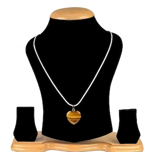May include: A heart-shaped pendant necklace with a tiger's eye stone. The pendant hangs from a white cord and is displayed on a black jewellery bust. The stone has brown and gold tones.