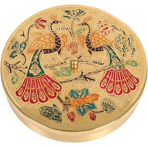 May include: A round, gold-colored decorative box with a detailed peacock design. The lid features two peacocks perched on a branch, with colorful tail feathers in red, green, and blue. The box has a small, gold knob on top.
