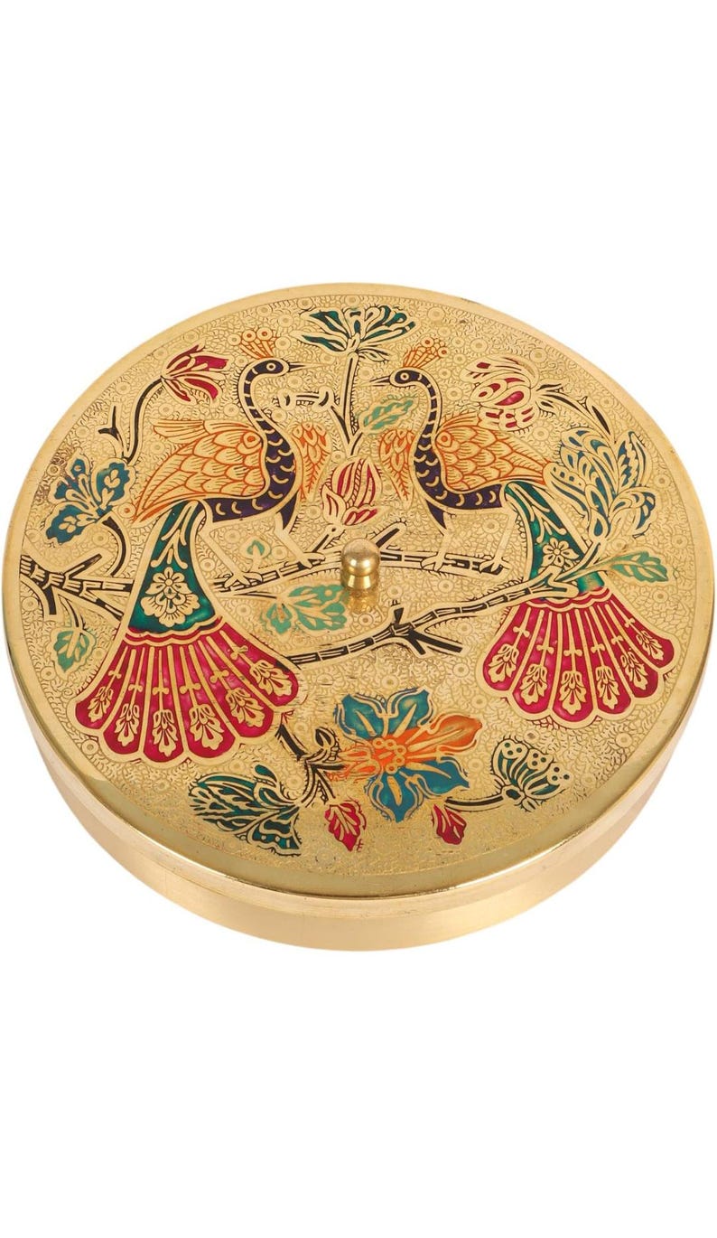 May include: A round, gold-colored decorative box with a detailed peacock design. The lid features two peacocks perched on a branch, with colorful tail feathers in red, green, and blue. The box has a small, gold knob on top.