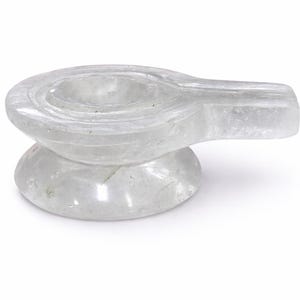 Pode incluir: Uma escultura em pedra clara e esculpida de um lingam, um símbolo de Shiva. A escultura tem uma base arredondada e um topo curvo e alongado com círculos concêntricos. A pedra é translúcida, com texturas internas visíveis.