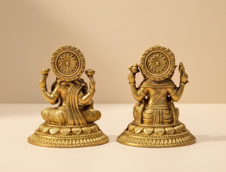 Pode incluir: Duas est&aacute;tuas douradas de uma divindade, vistas por tr&aacute;s. Cada est&aacute;tua tem uma aur&eacute;ola circular, roupas ornamentadas e est&aacute; sentada em uma base detalhada. As est&aacute;tuas est&atilde;o em uma superf&iacute;cie clara contra um fundo neutro.