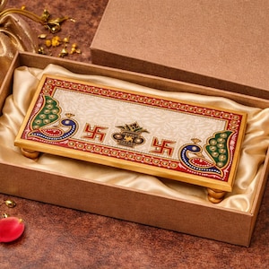 Pu&ograve; includere: Un vassoio rettangolare decorativo in marmo con una cornice in legno color oro, con pavoni e simboli religiosi. Il vassoio &egrave; presentato in una scatola marrone con fodera in raso. La scatola &egrave; aperta, rivelando il vassoio e un sacchetto dorato.