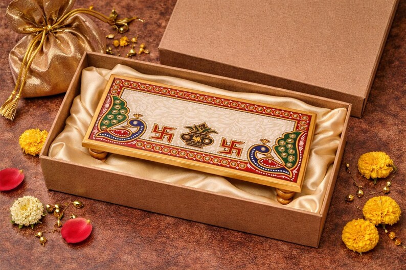 Pu&ograve; includere: Un vassoio rettangolare decorativo in marmo con una cornice in legno color oro, con pavoni e simboli religiosi. Il vassoio &egrave; presentato in una scatola marrone con fodera in raso. La scatola &egrave; aperta, rivelando il vassoio e un sacchetto dorato.