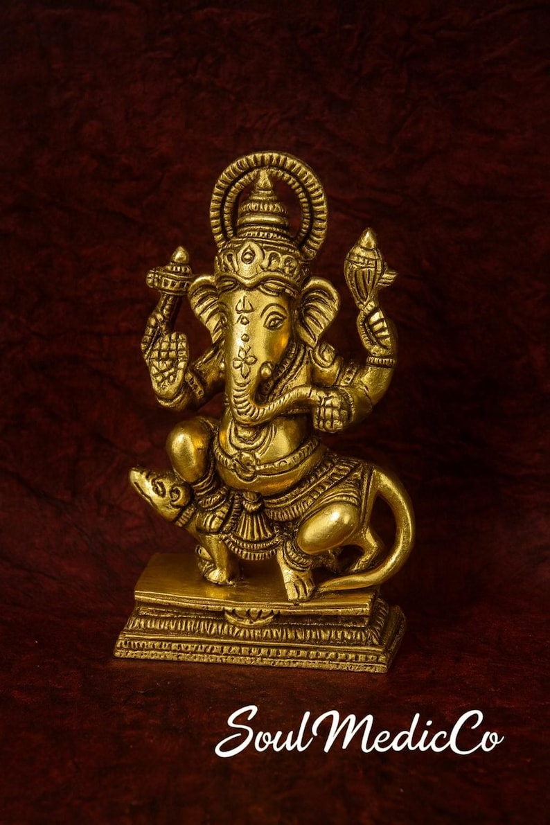 Op de afbeelding: Een goudkleurig beeld van de hindoe&iuml;stische god Ganesha, zittend op een rat. Het beeld heeft ingewikkelde details en staat op een rechthoekige basis. De tekst "Soul MedicCo" is onderaan zichtbaar.