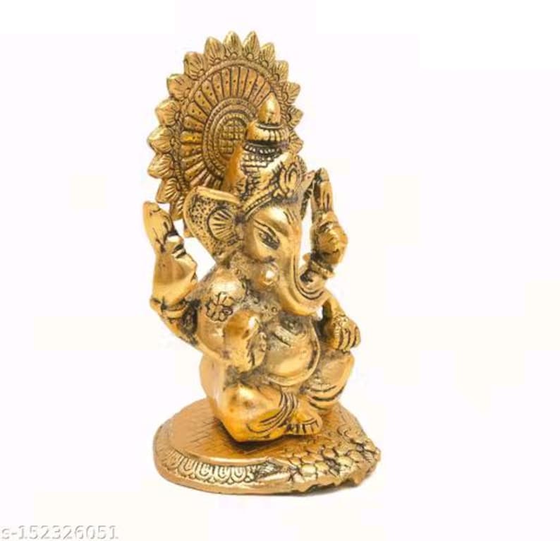 May include: A metallic gold-colored brass figurine of the deity Ganesha, depicted in a seated position with four arms, a prominent trunk, and large ears. The figure is set against a circular, sunburst-style halo and rests on a textured base.