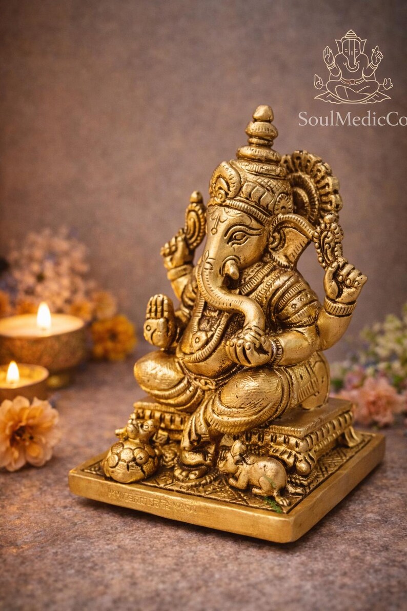 May include: A golden statue of the Hindu deity Ganesha, seated on a square base. The statue features intricate details, including a large elephant head, multiple arms, and ornate clothing. The background includes candles and flowers.