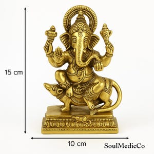 Op de afbeelding: Goudkleurig beeld van de hindoe-godheid Ganesha, zittend op een rat. Het beeld is 15 cm hoog en 10 cm breed. Ganesha wordt afgebeeld met een olifantenkop en meerdere armen, die verschillende voorwerpen vasthouden. De basis is rechthoekig en gedetailleerd.