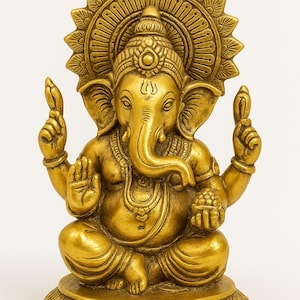 May include: A gold-colored brass statue of the deity Ganesha in a seated position. The figure features an elephant head, four arms, and a large circular halo behind the head. Ganesha sits on a circular base decorated with carved floral patterns.