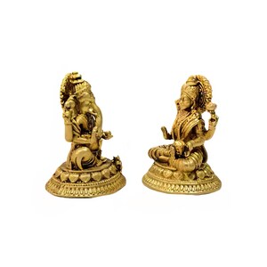 Pode incluir: Duas est&aacute;tuas douradas de divindades hindus. Uma est&aacute;tua retrata uma figura sentada com v&aacute;rios bra&ccedil;os e um adorno de cabe&ccedil;a ornamentado. A outra est&aacute;tua mostra uma figura com uma cabe&ccedil;a grande e v&aacute;rios bra&ccedil;os, sentada sobre uma base detalhada. Ambas as est&aacute;tuas est&atilde;o em fundo branco.