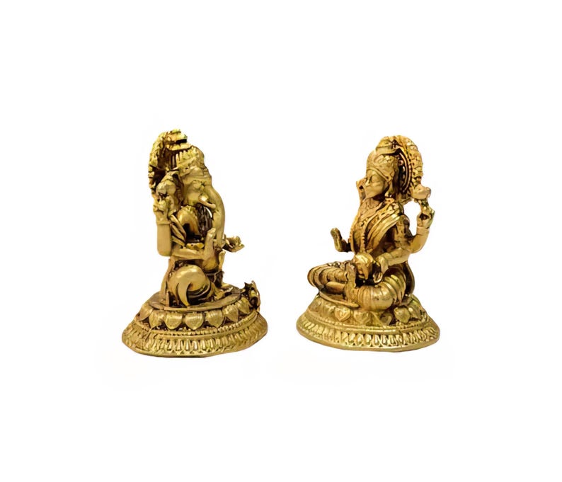 Pode incluir: Duas est&aacute;tuas douradas de divindades hindus. Uma est&aacute;tua retrata uma figura sentada com v&aacute;rios bra&ccedil;os e um adorno de cabe&ccedil;a ornamentado. A outra est&aacute;tua mostra uma figura com uma cabe&ccedil;a grande e v&aacute;rios bra&ccedil;os, sentada sobre uma base detalhada. Ambas as est&aacute;tuas est&atilde;o em fundo branco.