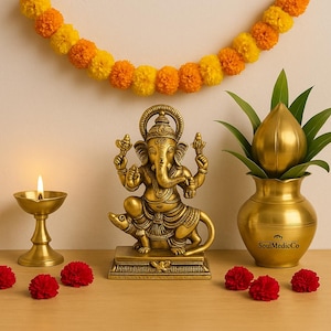 Op de afbeelding: Een gouden messing beeld van de hindoe-god Ganesha, zittend op een rat, met een brandende olielamp en een decoratieve pot met een lotusknop. Op de achtergrond een slinger van oranje en gele bloemen en rode anjers.
