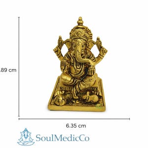 May include: A golden-colored Ganesh statue, 3.5 inches tall and 2.5 inches wide, sits on a rectangular base. The deity has an elephant head and multiple arms. The statue is a representation of the Hindu god Ganesh.