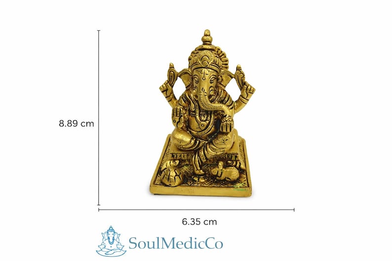 May include: A golden-colored Ganesh statue, 3.5 inches tall and 2.5 inches wide, sits on a rectangular base. The deity has an elephant head and multiple arms. The statue is a representation of the Hindu god Ganesh.