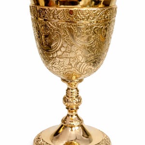 May include: A gold-colored chalice with intricate floral and scrollwork engravings. The chalice has a wide, detailed base, a slender stem, and a flared cup. The overall design is ornate and elegant, with a polished finish.