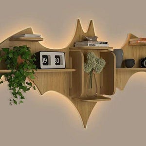 Pu&ograve; includere: Un ripiano a muro in legno a forma di pipistrello con pi&ugrave; ripiani. Il ripiano &egrave; di colore marrone chiaro ed &egrave; decorato con un orologio, un vaso con fiori e libri.