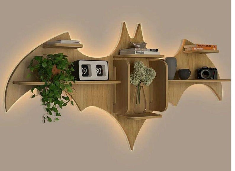 Pu&ograve; includere: Un ripiano a muro in legno a forma di pipistrello con pi&ugrave; ripiani. Il ripiano &egrave; di colore marrone chiaro ed &egrave; decorato con un orologio, un vaso con fiori e libri.