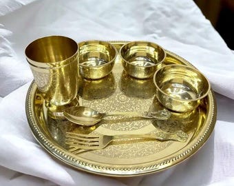 May include: A gold-toned brass serving set with a decorative plate, four bowls, a fork, and a spoon. The plate has an intricate floral design.