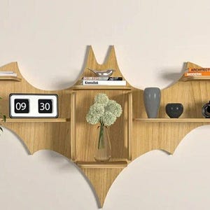 Pu&ograve; includere: Un ripiano a muro in legno a forma di pipistrello con cinque ripiani. I ripiani sono decorati con una pianta in vaso, un orologio che segna le 09:30, un vaso di fiori bianchi, una ciotola argentata, una macchina fotografica nera e argentata e due libri intitolati "Architettura" e "Moderno".