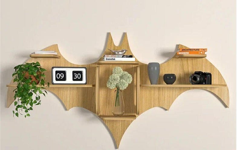 Pu&ograve; includere: Un ripiano a muro in legno a forma di pipistrello con cinque ripiani. I ripiani sono decorati con una pianta in vaso, un orologio che segna le 09:30, un vaso di fiori bianchi, una ciotola argentata, una macchina fotografica nera e argentata e due libri intitolati "Architettura" e "Moderno".