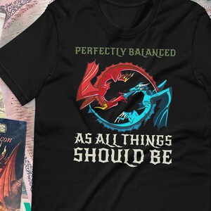 May include: Black t-shirt with a red and blue dragon design. The text "Perfectly Balanced As All Things Should Be" is printed on the shirt.