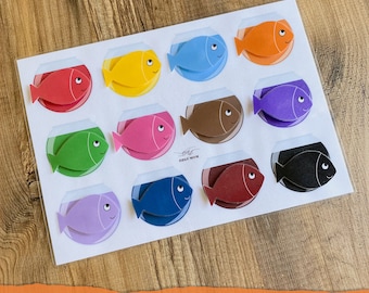 May include: A set of ten colorful fish shapes in a white frame. The fish are arranged in a circle and each fish is a different color: red, yellow, green, pink, brown, purple, blue, maroon, black, and orange. The frame has the text "COLOR ACTIVITY FISH" at the bottom.