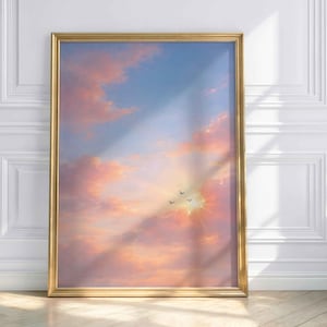 Könnte beinhalten: Ein gerahmter Kunstdruck mit einer Himmelsansicht bei Sonnenuntergang mit rosa und orangefarbenen Wolken, einer hellen Sonne und blauem Himmel. Drei Vögel sind gegen die Sonne silhouettiert. Der Rahmen ist goldfarben.