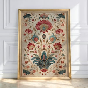 Puede incluir: Una obra de arte enmarcada con un diseño floral detallado en tonos rojos, turquesas y azules sobre un fondo crema. El marco dorado complementa el intrincado patrón, creando una estética vintage. La obra está apoyada contra una pared blanca.