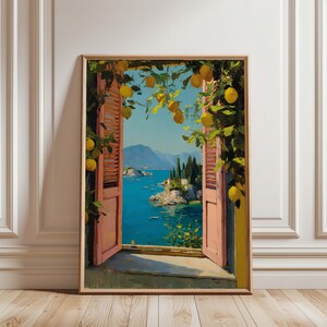 Könnte beinhalten: Ein gerahmter Kunstdruck zeigt eine Küstenlandschaft durch ein offenes Fenster. Das Kunstwerk zeigt ein leuchtend blaues Meer, entfernte Berge und Gebäude. Zitronenzweige mit gelben Früchten umrahmen das Fenster und verleihen der Szene einen natürlichen Touch. Die Fensterläden sind rosa.