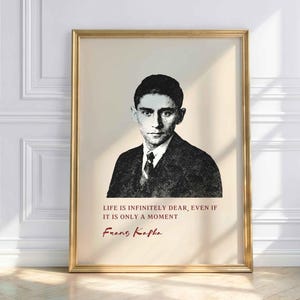 Könnte beinhalten: Ein gerahmter Kunstdruck mit einem schwarz-weißen Porträt von Franz Kafka auf cremefarbenem Hintergrund. Unter dem Porträt steht der Text: LIFE IS INFINITELY DEAR, EVEN IF IT IS ONLY A MOMENT, gefolgt von der Signatur Franz Kafka in Rot.