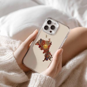 May include: Clear phone case featuring a colorful map design with a sunburst in the center. The map is filled with intricate patterns in red, gold, and blue. The phone case is held in a person's hands.
