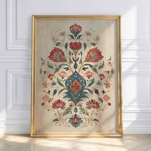 May include: A framed floral print with a gold frame. The artwork features a symmetrical design of red, pink, and teal flowers and leaves on a beige background. The print is leaning against a white wall and wooden floor.