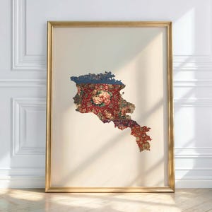 May include: A framed print featuring the outline of a country, filled with a floral pattern in red, blue, and beige. The print is set against a cream-colored background and framed in gold. The artwork is displayed on a white wall.