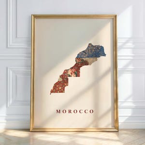 Pode incluir: Impressão artística emoldurada com o mapa de Marrocos, preenchida com desenhos florais e de tecido estampado em vermelho, azul e bege. A palavra "MOROCCO" está impressa em vermelho escuro na parte inferior. A moldura é dourada.