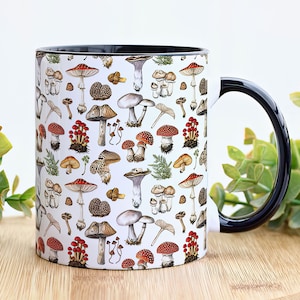 May include: A white ceramic mug with a black handle and a pattern of various mushrooms in shades of red, brown, and white. The mug is filled with a white liquid.