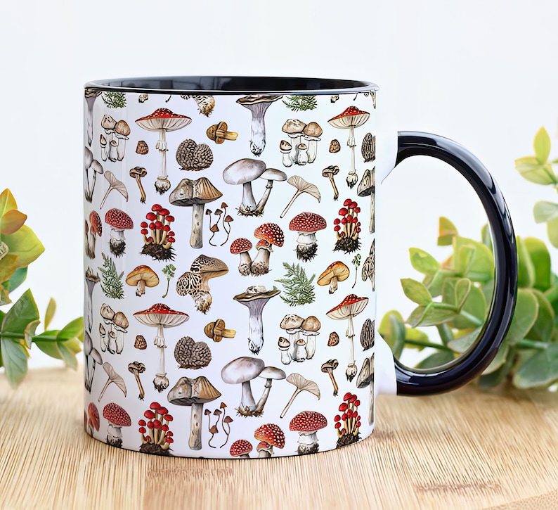May include: A white ceramic mug with a black handle and a pattern of various mushrooms in shades of red, brown, and white. The mug is filled with a white liquid.