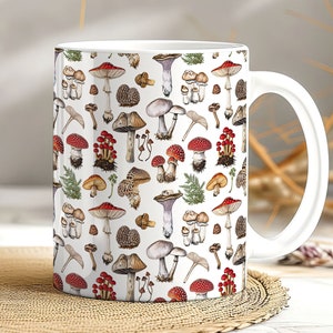 May include: White ceramic mug with a colorful mushroom pattern. The mug features a variety of mushrooms in different shapes, sizes, and colors, including red, brown, and white. The mushrooms are arranged in a repeating pattern on the mug.