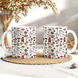 May include: Two white ceramic mugs with a colorful mushroom pattern. The mugs have a white background with a variety of mushrooms in different colors and sizes, including red, brown, white, and purple. The mushrooms are arranged in a random pattern.