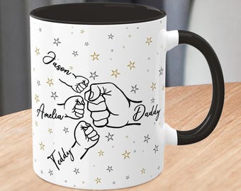 May include: White ceramic mug with a black interior and handle. The mug features a graphic of a fist bump with the names "Jason", "Amelia", "Teddy", and "Daddy" written in script. Gold and black stars are scattered across the mug.