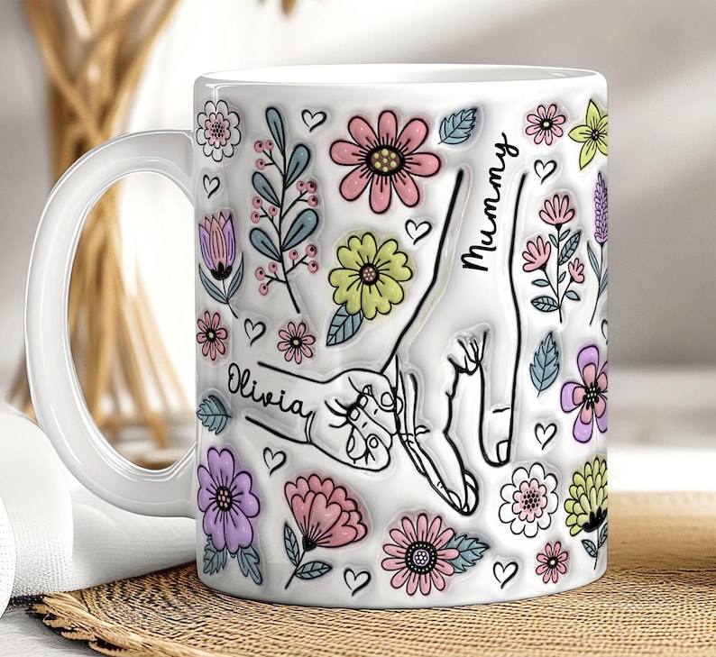 May include: White ceramic mug with a floral design and the words "Mummy" and "Olivia" printed on it. The design features a handprint of a mother and child holding hands.
