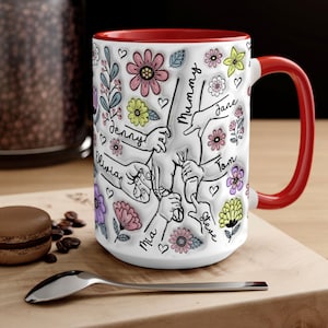 May include: White ceramic mug with a red rim and handle. The mug features a colourful floral design with hand-drawn illustrations of hands holding a stick and the names "Mummy", "Denny", "Olivia", "Mia", "Jane", "Tom", and "Steve".