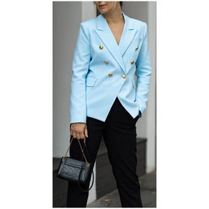 May include: A light blue blazer with gold buttons, paired with black trousers and a small black handbag. The blazer features a double-breasted design and a classic lapel. The handbag has a chain strap.