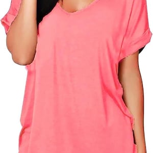 May include: A coral V-neck t-shirt with short, rolled sleeves. The top has a loose fit and is worn with black trousers. The material looks soft and lightweight, ideal for everyday wear.