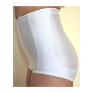 May include: A high-waisted white shaper brief featuring a smooth, satin-like finish with vertical stitched paneling along the sides. The garment has a scalloped edge trim along the waistband and leg openings, providing a structured fit.